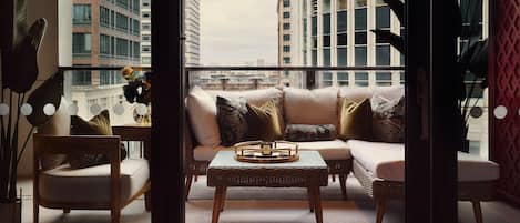 A balcony with a sofa, chairs, and a table, overlooking a cityscape.