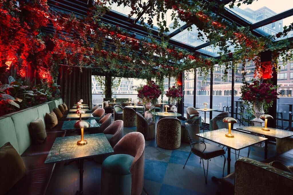 An indoor seating area with tables and chairs, a glass ceiling, and red foliage.