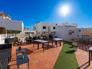 Une terrasse sur le toit avec des sièges extérieurs, un petit jardin et des bâtiments blancs en arrière-plan.