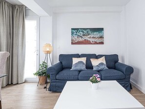 Uma sala de estar moderna com um sofá azul, uma mesa de centro branca e um quadro na parede.