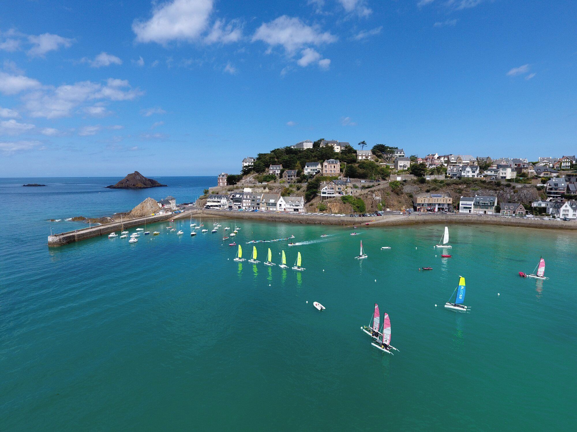 Une ville côtière dotée d’un port de plaisance, de maisons construites sur une colline et d’une eau d’un bleu limpide.