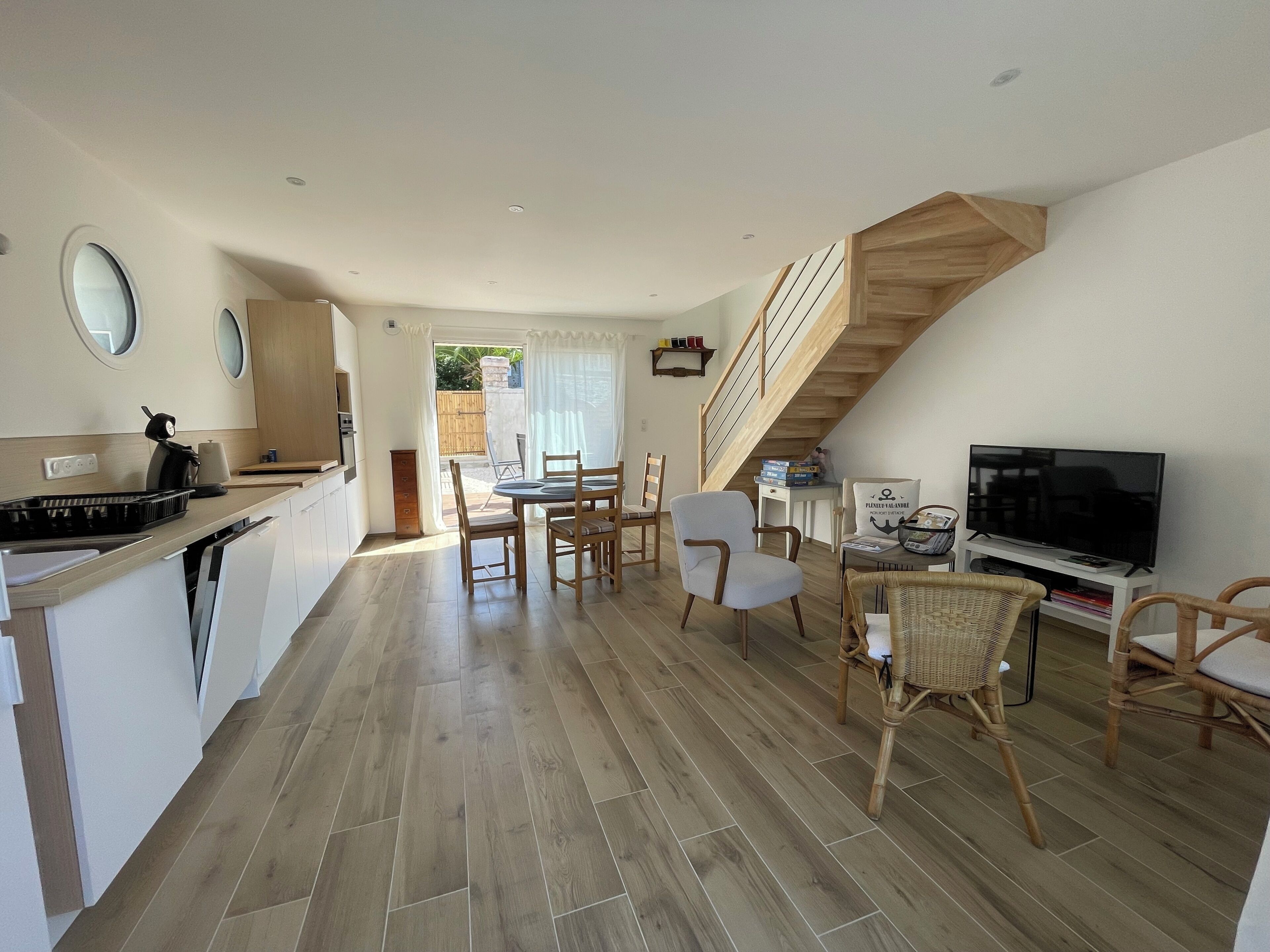 A modern kitchen with a dining area, a TV, and a staircase.