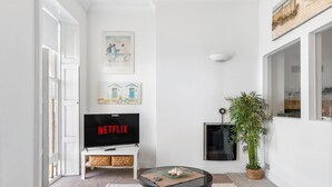 Ein Wohnzimmer mit Flachbildfernseher, der 'NETFLIX' anzeigt, einem weißen Sofa, einem Couchtisch und einem Blumentopf.