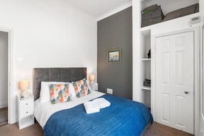 A bedroom with a bed, bedside lamps, a nightstand, a wall-mounted painting, and a wardrobe. - Seaview Haven By My Getaways (Brighton)