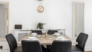 Ein Essbereich mit einem rechteckigen Tisch, sechs Stühlen, einer Wandleuchte und einem Wandbild.