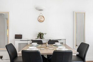 A dining area with a rectangular table, six chairs, a wall-mounted light fixture, and a decorative wall hanging. - Seaview Haven By My Getaways (Brighton)