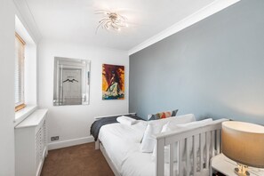 A bedroom with a bed, a nightstand, a lamp, a window with blinds, a door, and a painting on the wall. - Seaview Haven By My Getaways (Brighton)