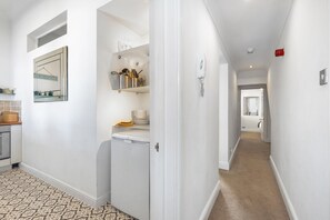 A hallway with a kitchen area on the left, a white refrigerator, and a door leading to another room. - Seaview Haven By My Getaways (Brighton)