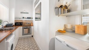 Eine kleine Küche mit Mikrowelle, Toaster und Backofen. Regale mit Küchenutensilien und ein Schild mit der Aufschrift 'Welcome to Beach House'.