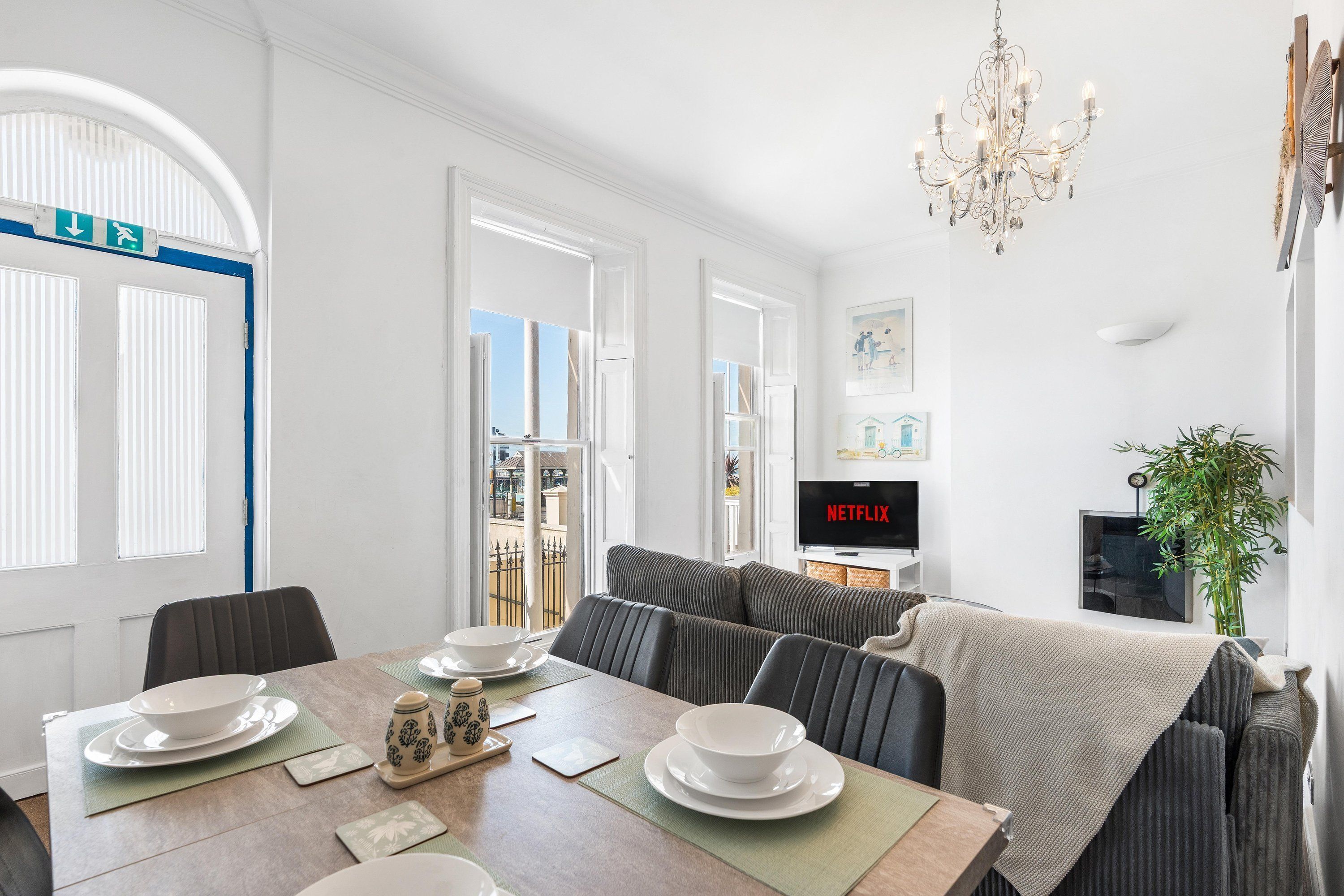 A modern living room with a dining area, a chandelier, a television, and a view of the outside.