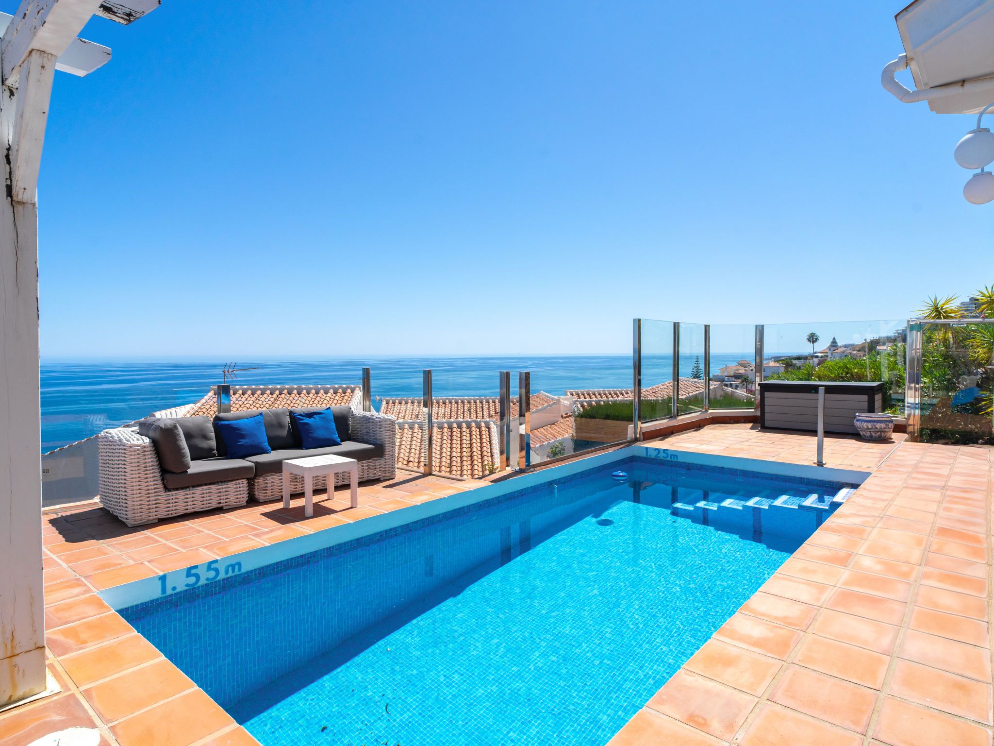 Ein Pool auf dem Dach mit freiem Blick auf den Ozean, eine Sitzecke mit Kissen und eine geflieste Terrasse.