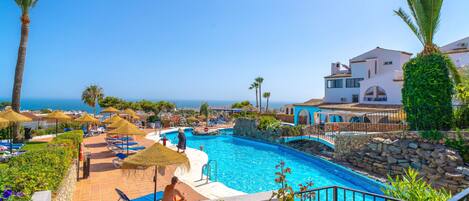 A resort pool area with a view of the sea, lounge chairs, and a lifebuoy.