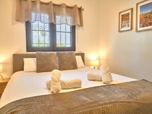 A hotel room with a bed, two bedside lamps, a window with curtains, and two framed pictures on the wall. - Casa Sofia Capistrano Village Pueblo 110B by Interhome (Nerja)