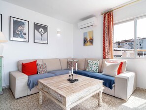 Ein modernes Wohnzimmer mit einem beigefarbenen Sofa, einem Couchtisch und Blick auf eine Stadtlandschaft durch das Fenster.