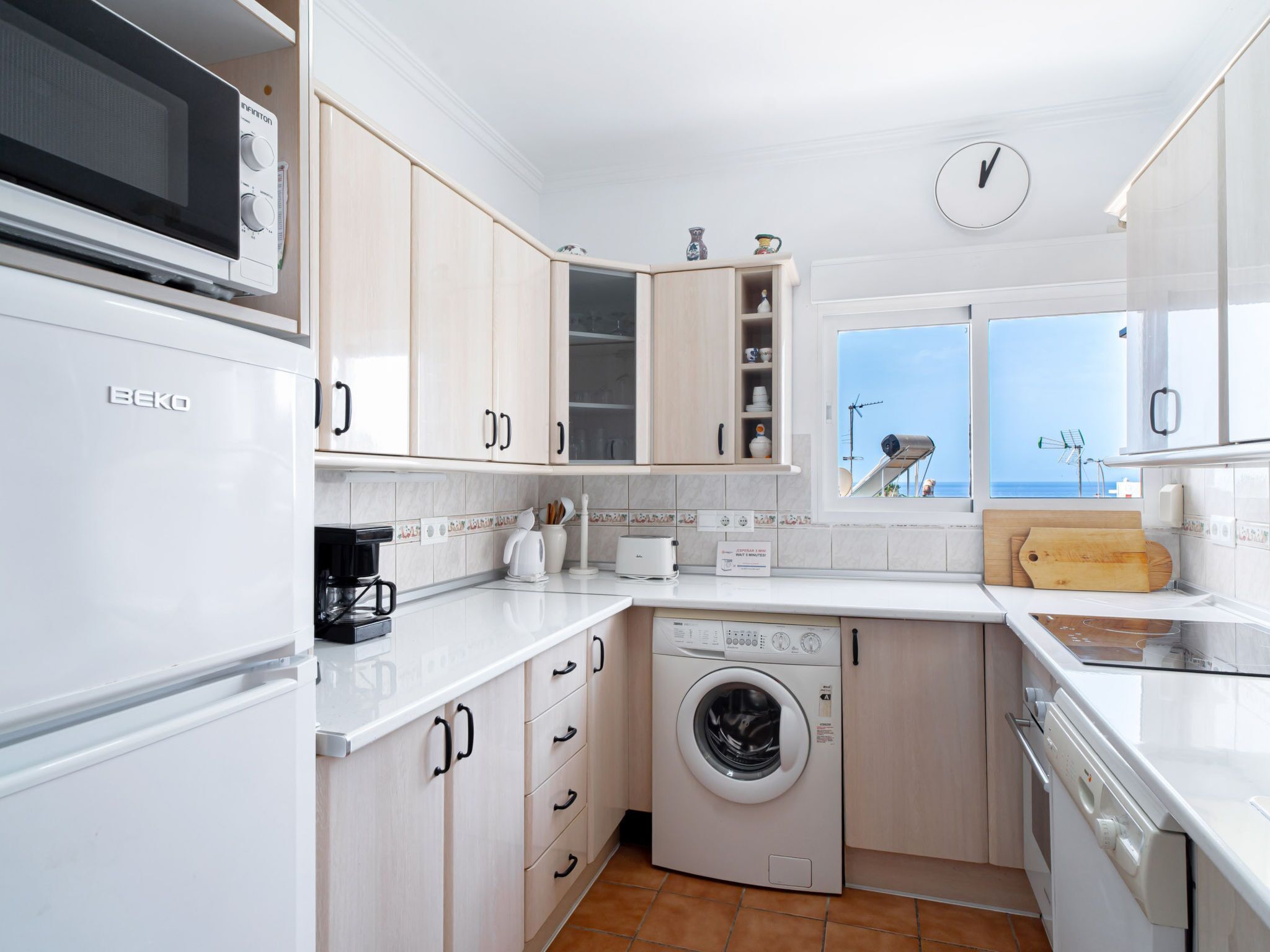 Een functionele keuken met een wasmachine, een magnetron en een koffiezetapparaat.