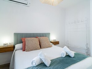 Ein ordentlich gemachtes Bett mit einer grünen Tagesdecke, zwei Kissen und aufgerollten Handtüchern.
