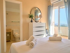 Habitación de hotel con cama, cómoda, espejo, inodoro y balcón con vistas.