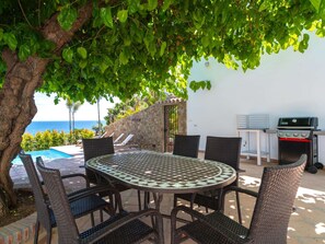 An outdoor dining area with a round table and wicker chairs, a barbecue grill, and a view of the sea. - Villa Lorca Vista Mar by Casasol by Interhome (Nerja)
