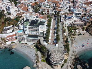 Un hotel frente al mar con varios pisos, un patio central y una zona de playa con sombrillas.