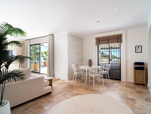 A modern living room with a sofa, a dining table with chairs, a large potted plant, and a view through a glass door. - Villa La Casita Fuente del Baden 52 by Casasol by Interhome (Nerja)
