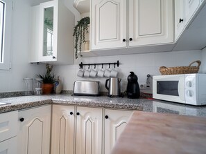 A kitchen with white cabinets, a countertop with a toaster, a kettle, a coffee maker, and a microwave. - Villa La Casita Fuente del Baden 52 by Casasol by Interhome (Nerja)