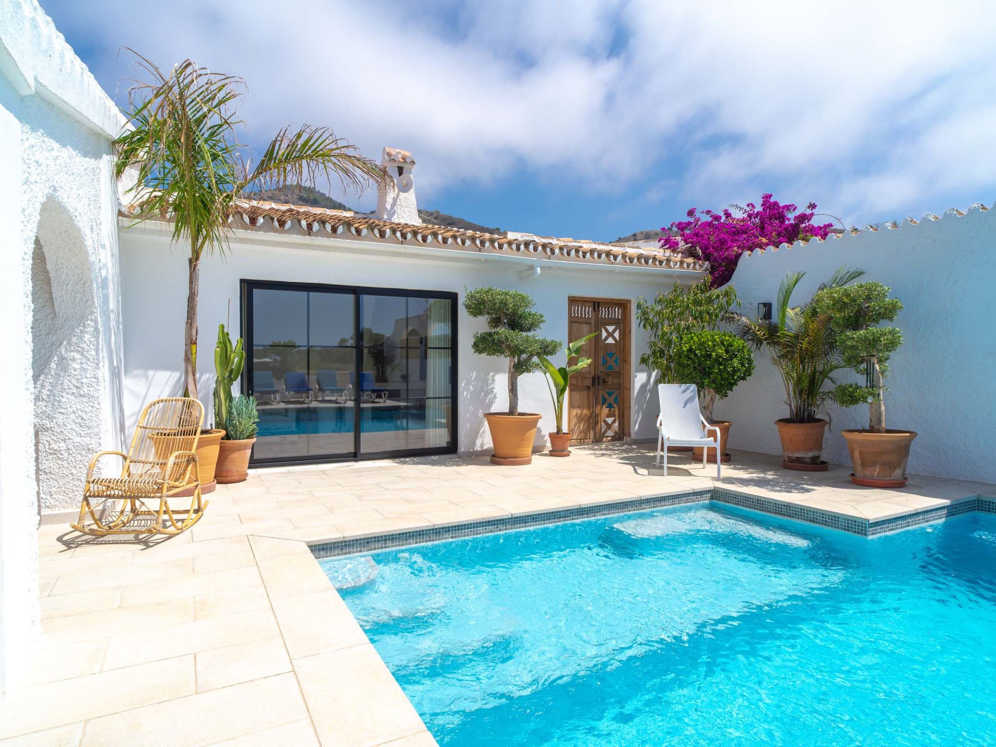 A poolside area with a clear blue pool, potted plants, and outdoor furniture.