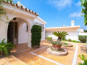 A white building with a tiled roof, a covered entrance, and a garden with potted plants and a palm tree. - Villa La Casita Fuente del Baden 52 by Casasol by Interhome (Nerja)