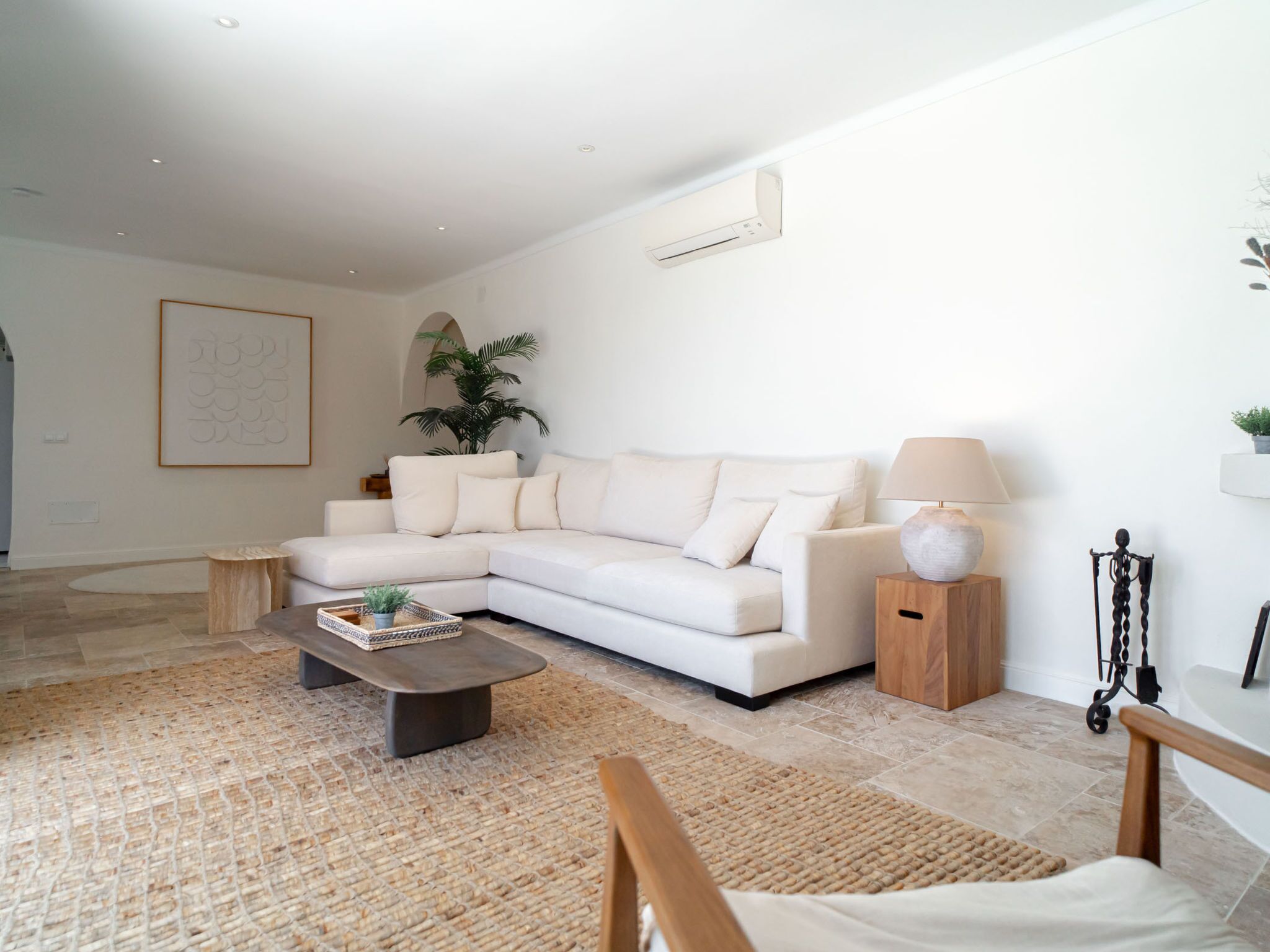 Uma sala de estar moderna com um sofá branco, uma mesa de centro, um abajur e uma planta decorativa.