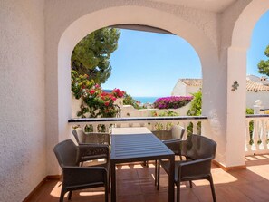 Eine Terrasse im Freien mit Tisch und Stühlen, Blick auf das Meer und ein Balkon mit Pflanzen.