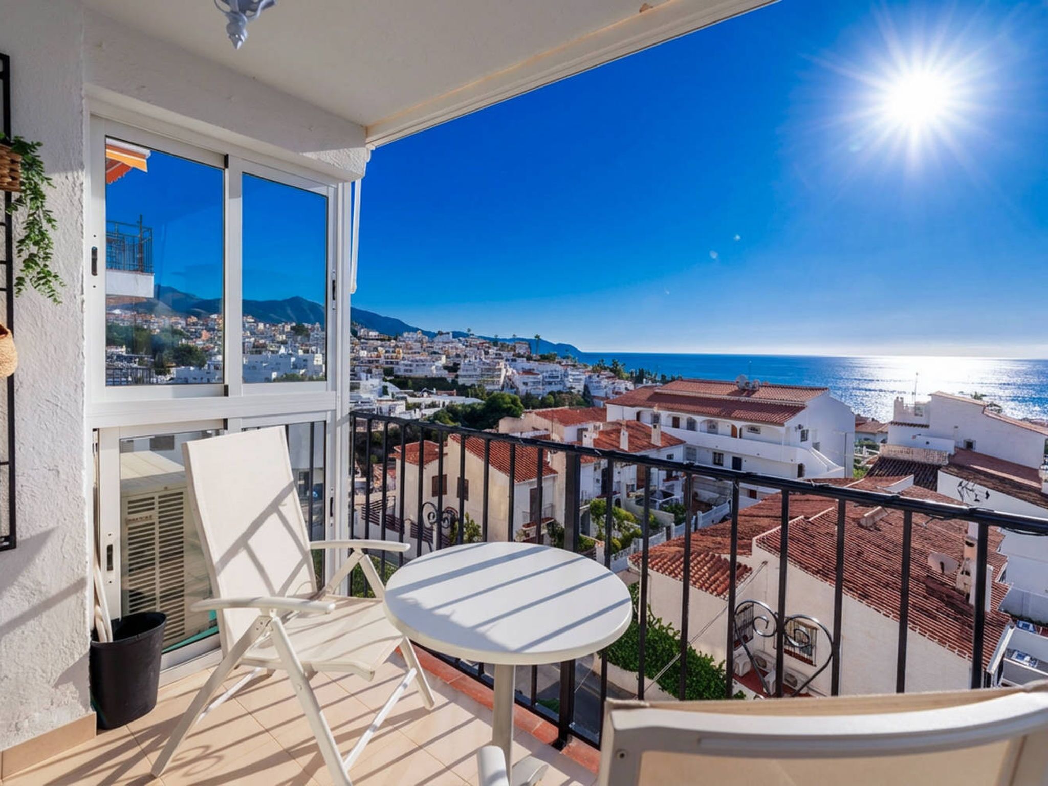 Un balcon avec une table et des chaises, donnant sur une ville côtière et la mer.