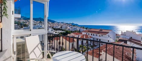 Un balcon avec une table et des chaises, donnant sur une ville côtière et la mer.