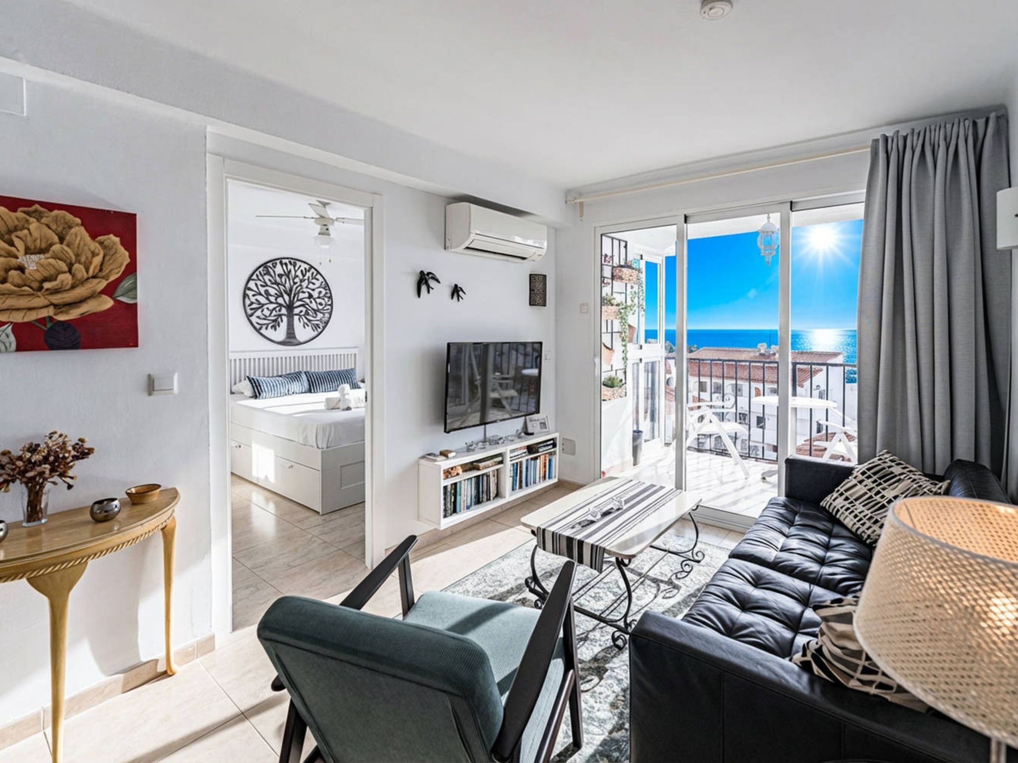 A modern living room with a balcony, a flat-screen TV, and a view of the sea.
