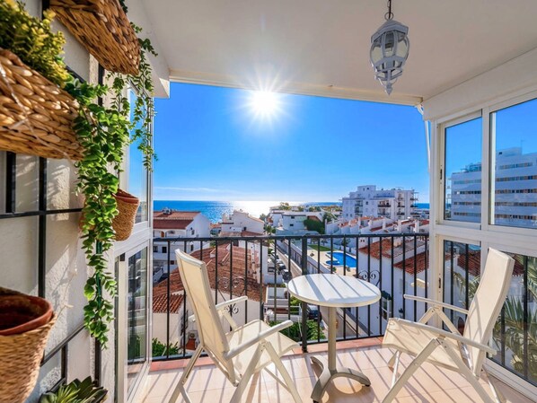 Ein Balkon mit Tisch und Stühlen, der Blick auf die Küste mit Gebäuden und einem klaren Himmel bietet.