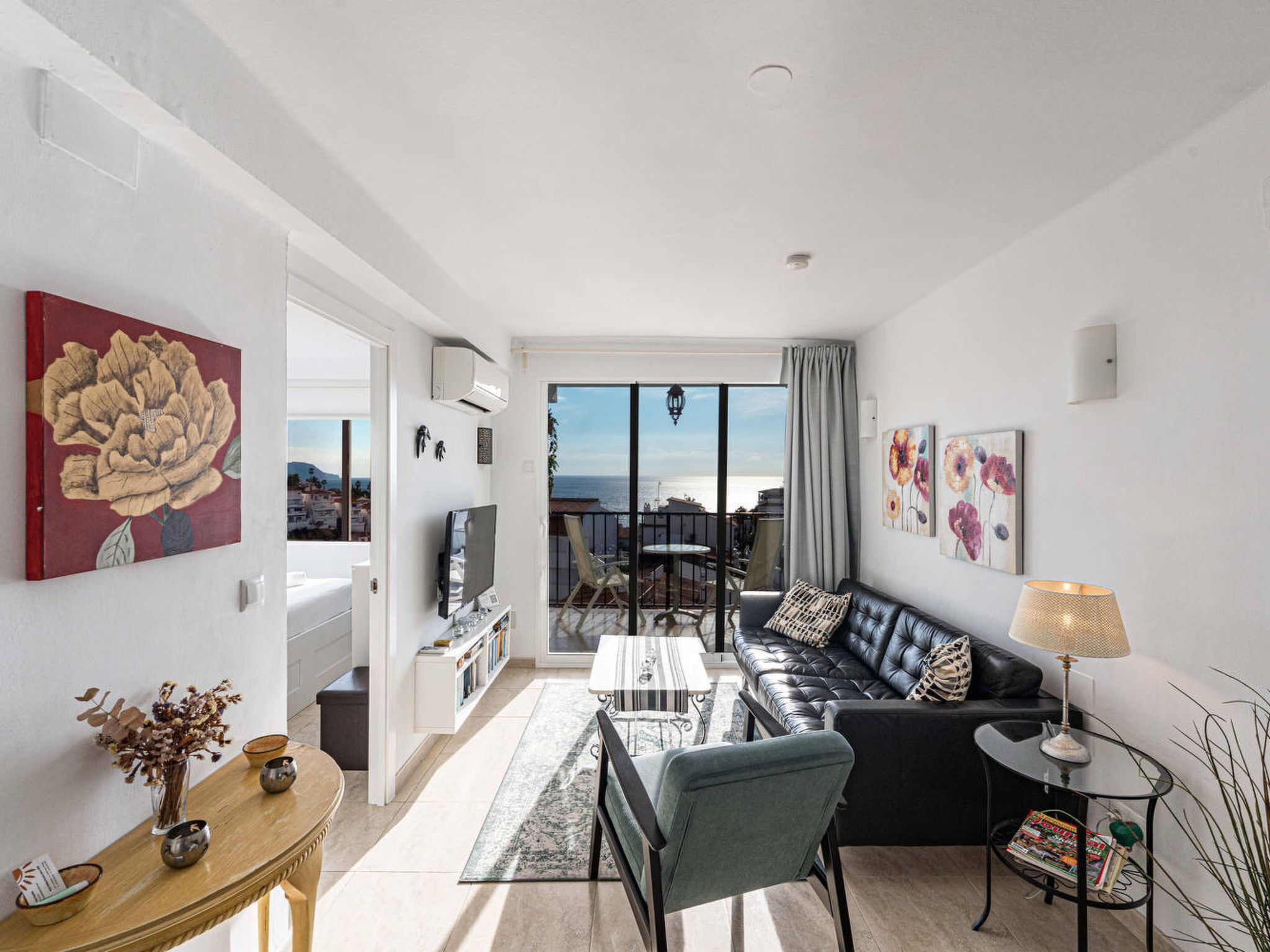 Uma sala de estar moderna com um sofá de couro preto, uma área de jantar e vista para o mar através de grandes janelas.