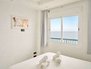 Une chambre d’hôtel avec un lit, une fenêtre donnant sur la mer, un tableau au mur et une prise électrique.