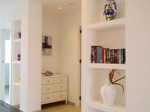 Een hal met een witte dressoir, een boekenkast vol boeken, een vaas met een plant en een schilderij aan de muur.