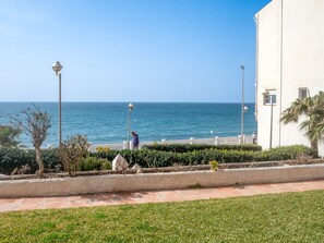 Ein Küstenweg mit Blick auf das Meer, ein weißes Gebäude und eine Person, die spazieren geht.