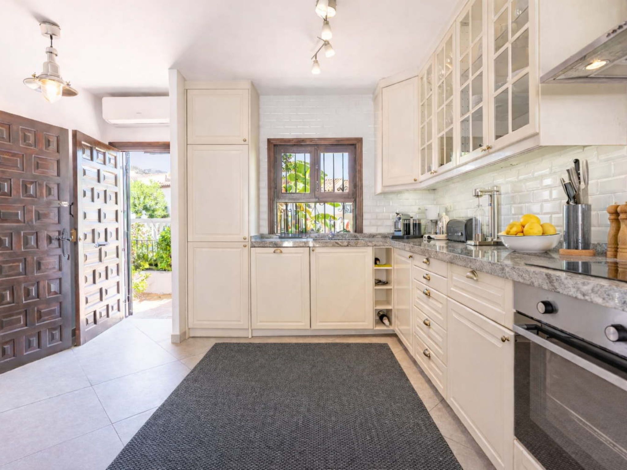 A kitchen with white cabinets, a granite countertop, and a window with a view of greenery.