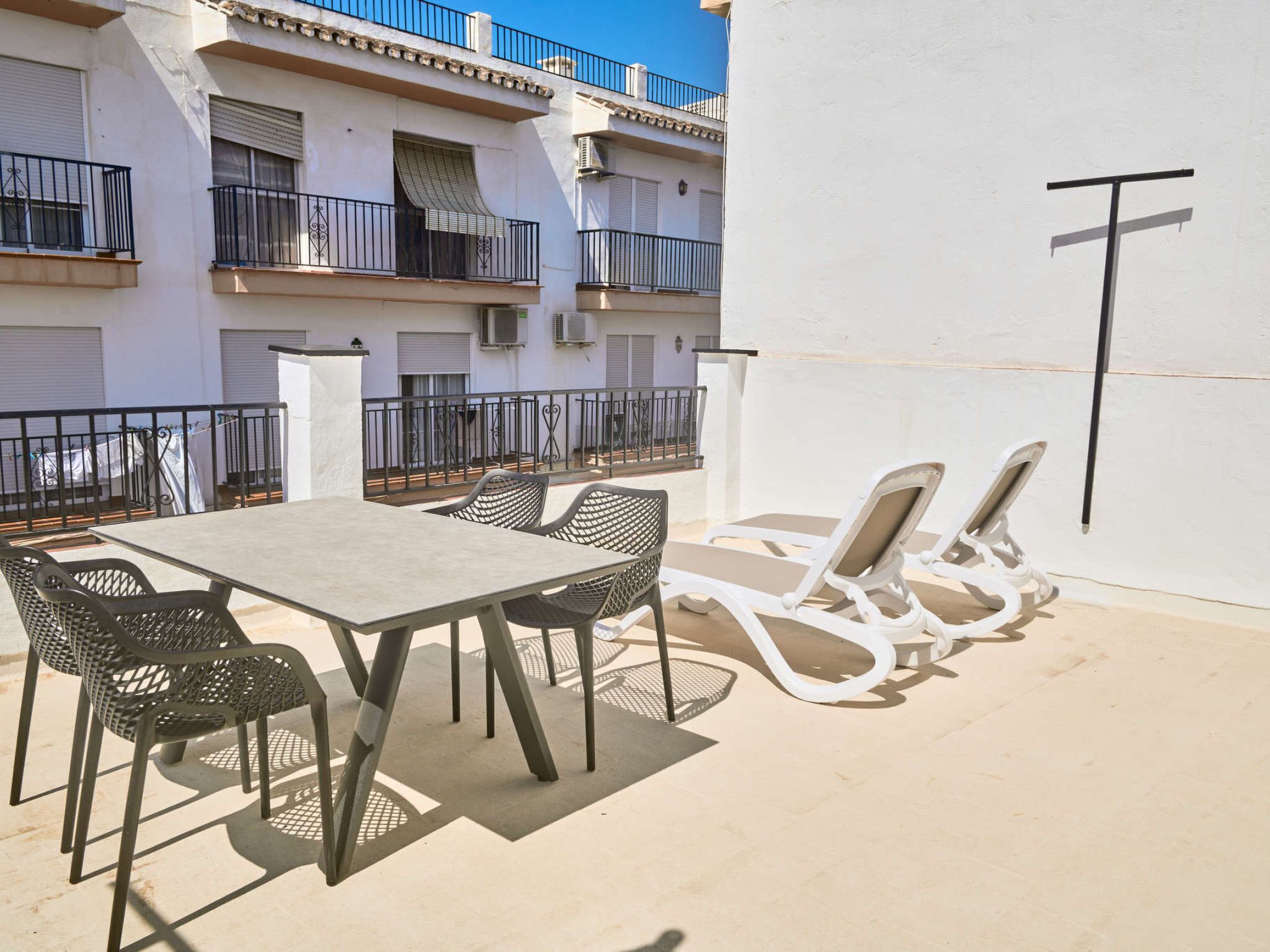 Une terrasse extérieure avec une table et des chaises, un mur blanc et une balustrade de balcon.