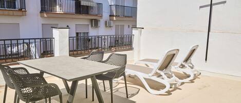 Une terrasse extérieure avec une table et des chaises, un mur blanc et une balustrade de balcon.