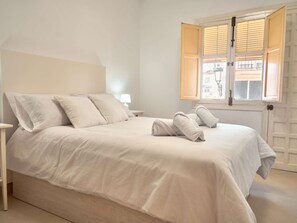 A bedroom with a bed, pillows, a nightstand, a lamp, and a window with blinds. - Casa Chica Calle Cristo 112 by Casasol by Interhome (Nerja)