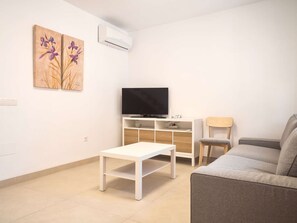 A living room with a flat-screen TV, a white coffee table, a grey sofa, a wooden cabinet, and two paintings on the wall. - Casa Chica Calle Cristo 112 by Casasol by Interhome (Nerja)