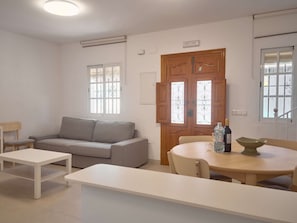A minimalist living room with a sofa, a dining table with chairs, and a wooden door with glass panels. - Casa Chica Calle Cristo 112 by Casasol by Interhome (Nerja)