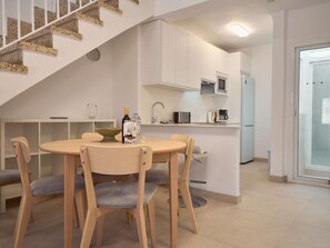 A modern kitchen with white cabinets, a microwave, and a refrigerator. There is a dining area with a round table and four chairs. - Casa Chica Calle Cristo 112 by Casasol by Interhome (Nerja)
