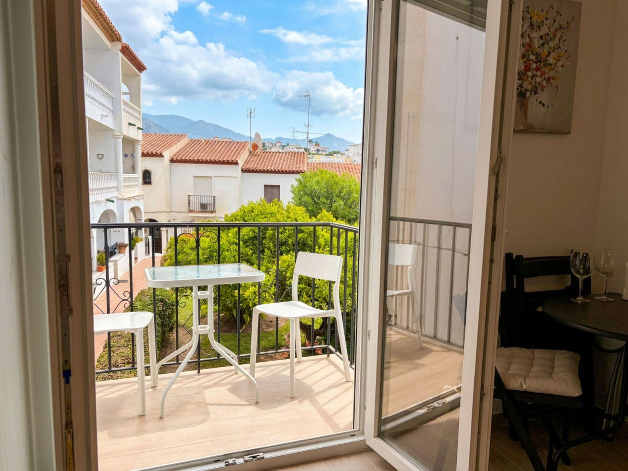 Un balcon avec une table et des chaises, une vue sur les bâtiments et les montagnes, et un coin repas avec une table et des chaises.