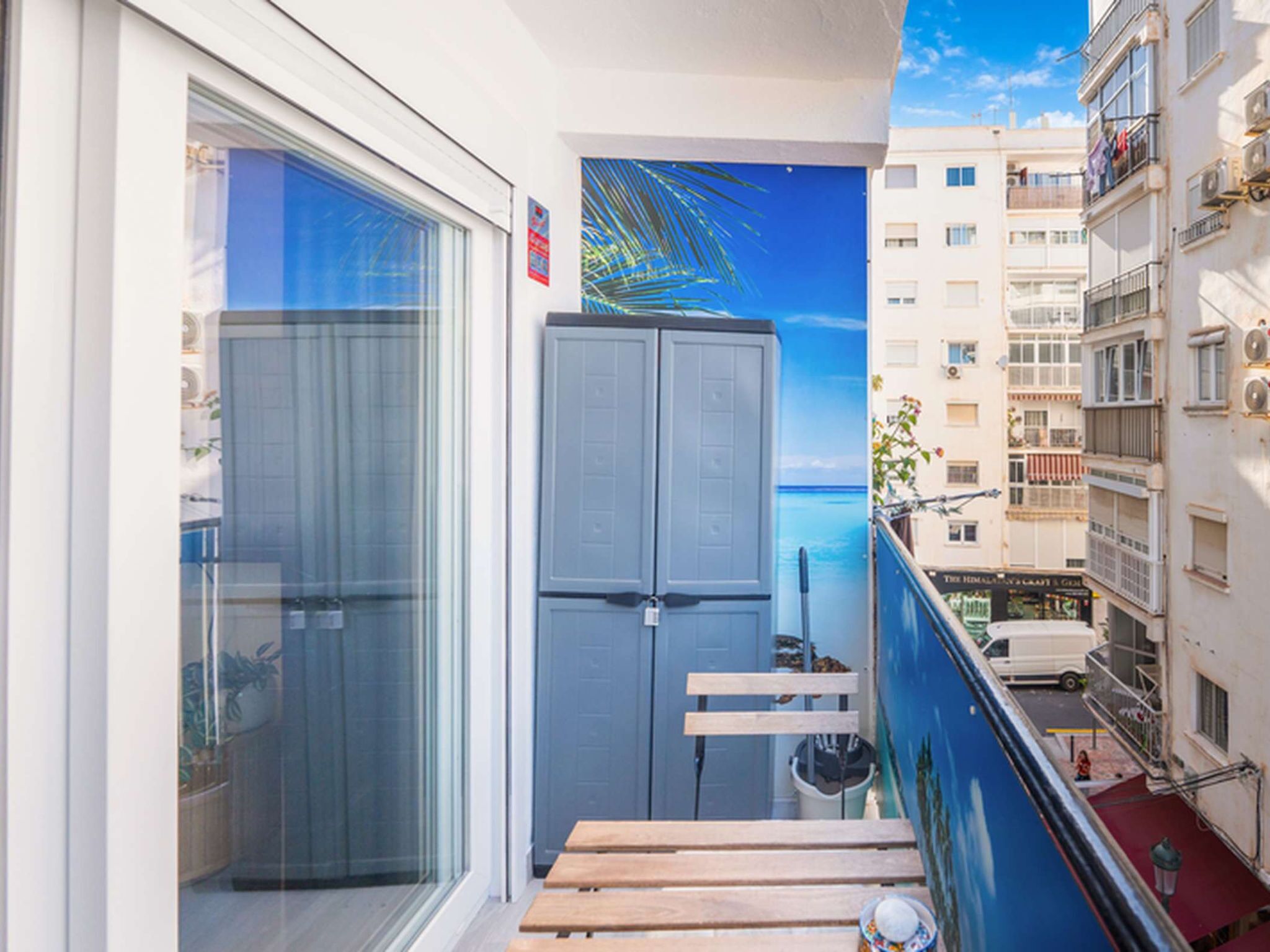 A balcony with a view of the sea, a grey cabinet, and a wooden bench.