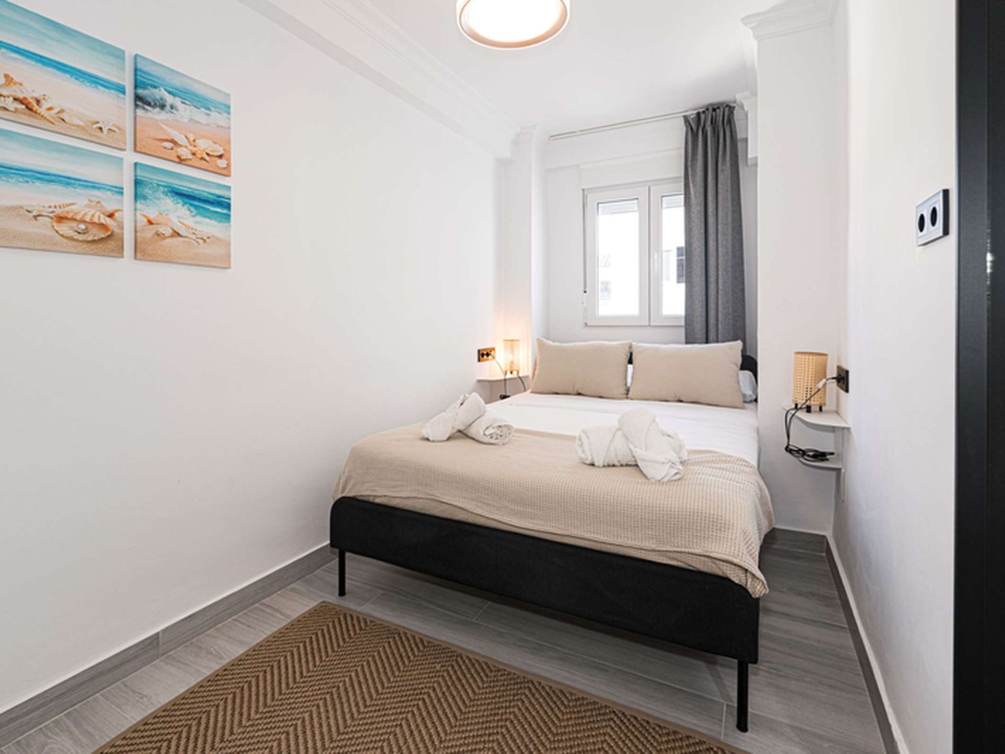 A hotel room with a bed, a nightstand, a lamp, and a window with curtains.