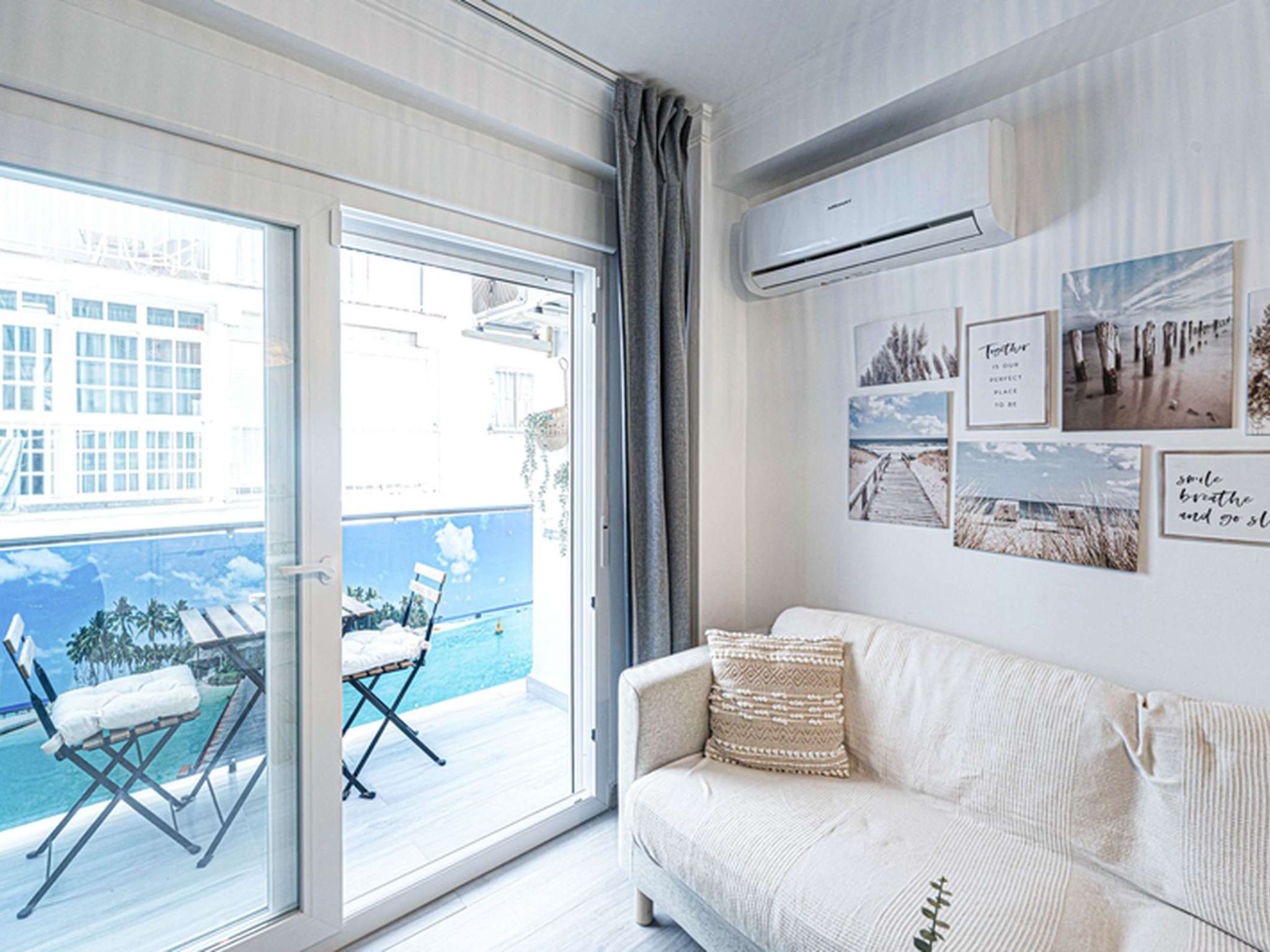 A room with a white sofa, a balcony with a pool, and a city view.