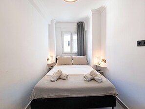 A hotel room with a bed, two bedside lamps, a window with curtains, and a towel on the bed. - Apartment  by Interhome (Nerja)