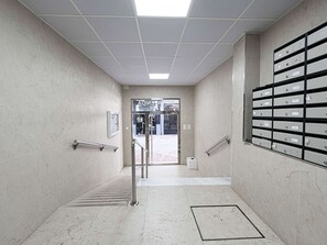 A hallway with a tiled floor, metal handrails, a door leading to an outdoor area, and a wall-mounted filing cabinet. - Apartment  by Interhome (Nerja)